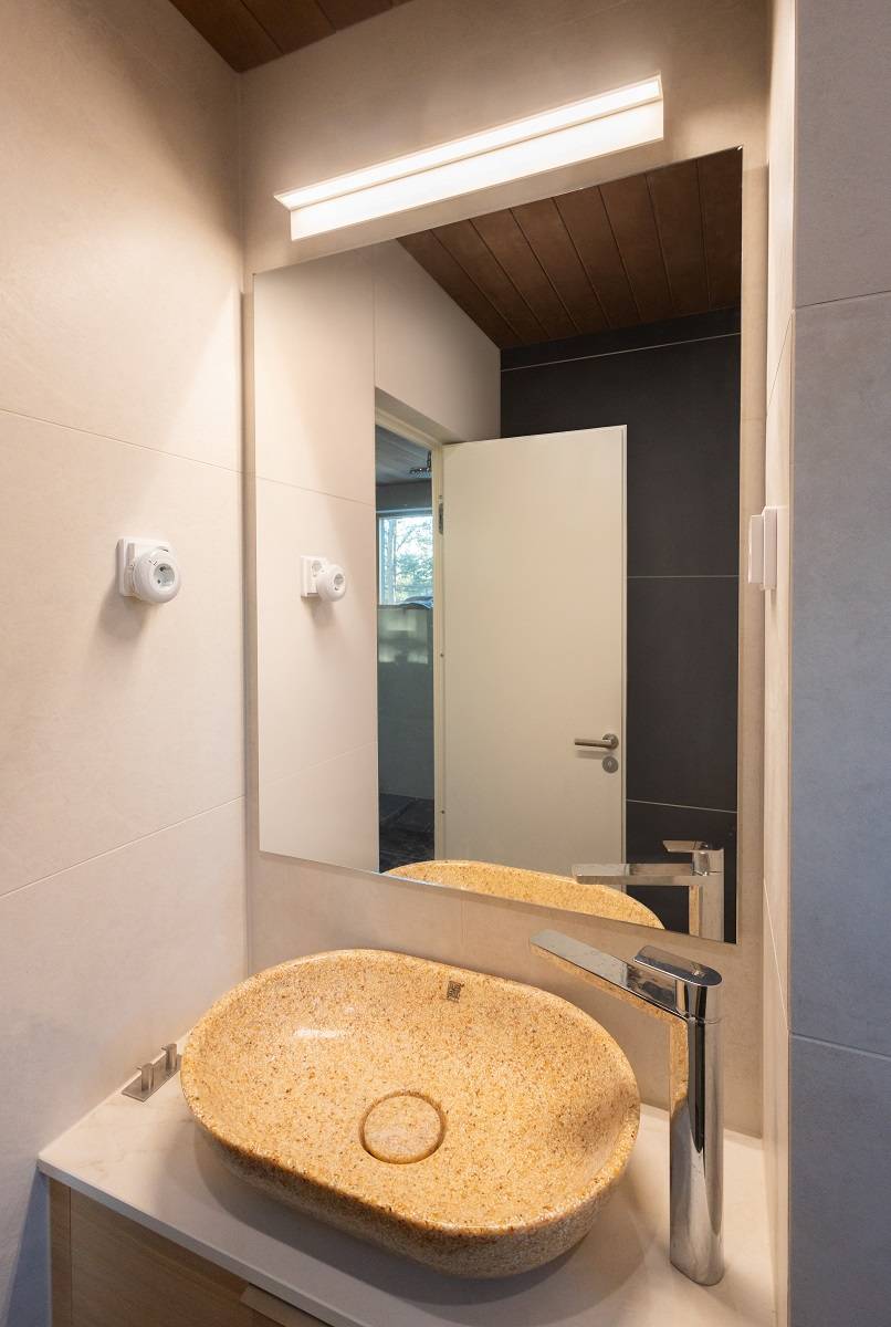 Na malé toaletě minimalistické bílé nástěnné svítidlo o délce 60 cm elegantně osvětluje zrcadlo. Světlo má barevnou teplotu 3 000 kelvinů.